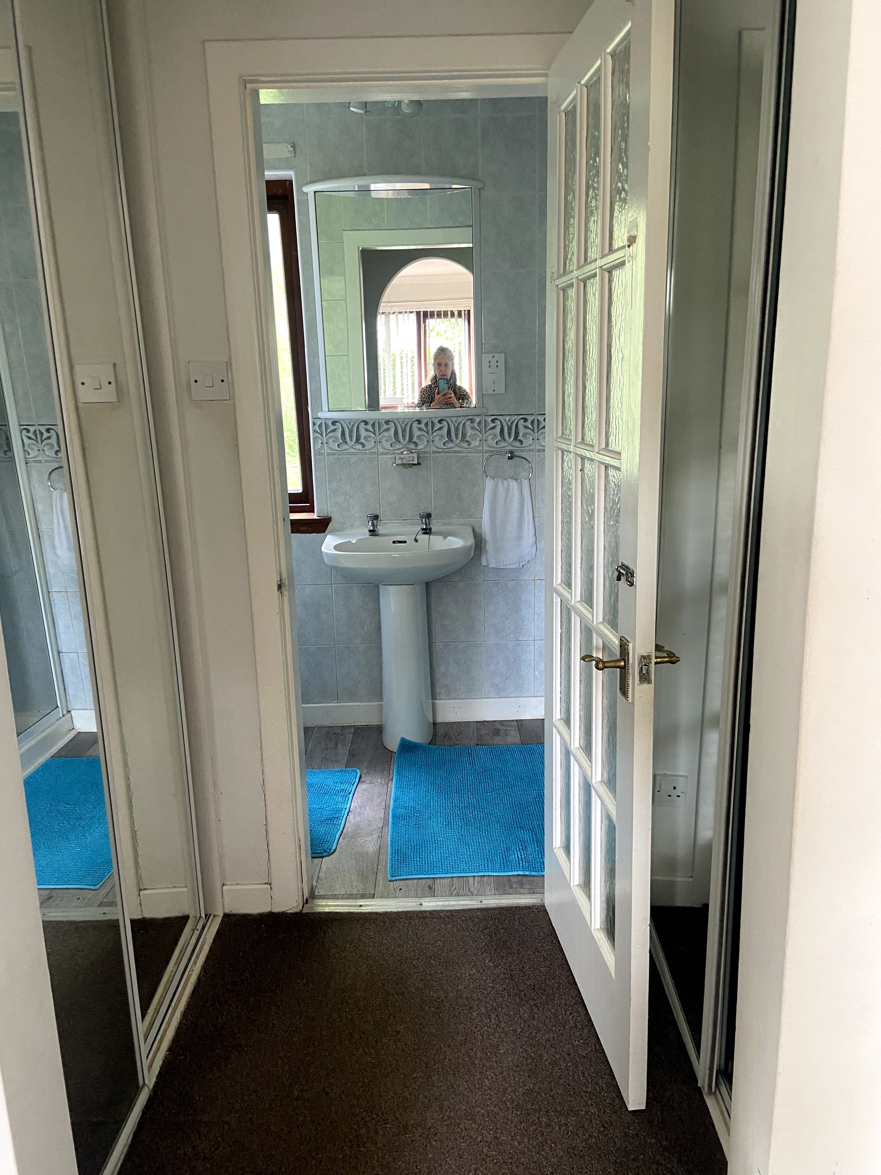 A bathroom with a sink, mirror, and blue mats on the floor.