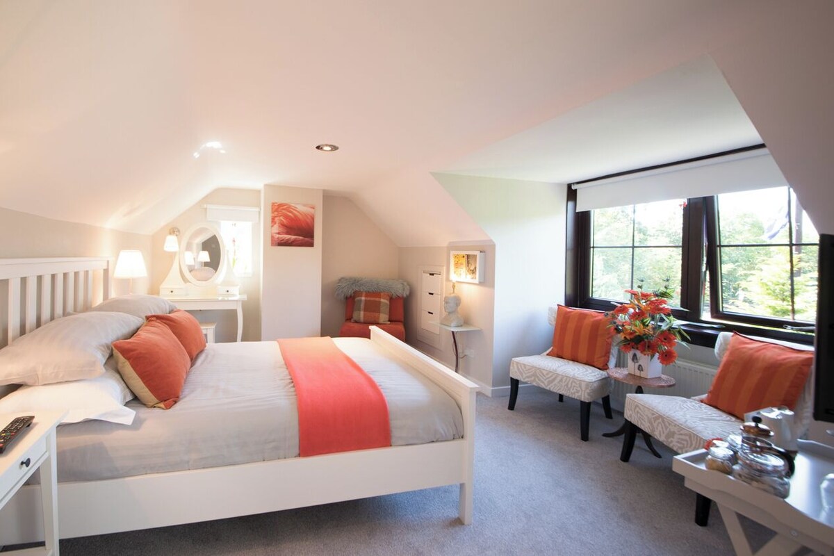 A bedroom with a bed, bedside tables, a desk, a chair, and a window.