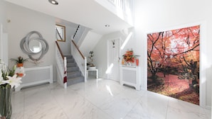 A spacious foyer with a marble floor, a white staircase, a decorative mirror, and a large window with a view of autumn trees. - JustB (Edinburgh)