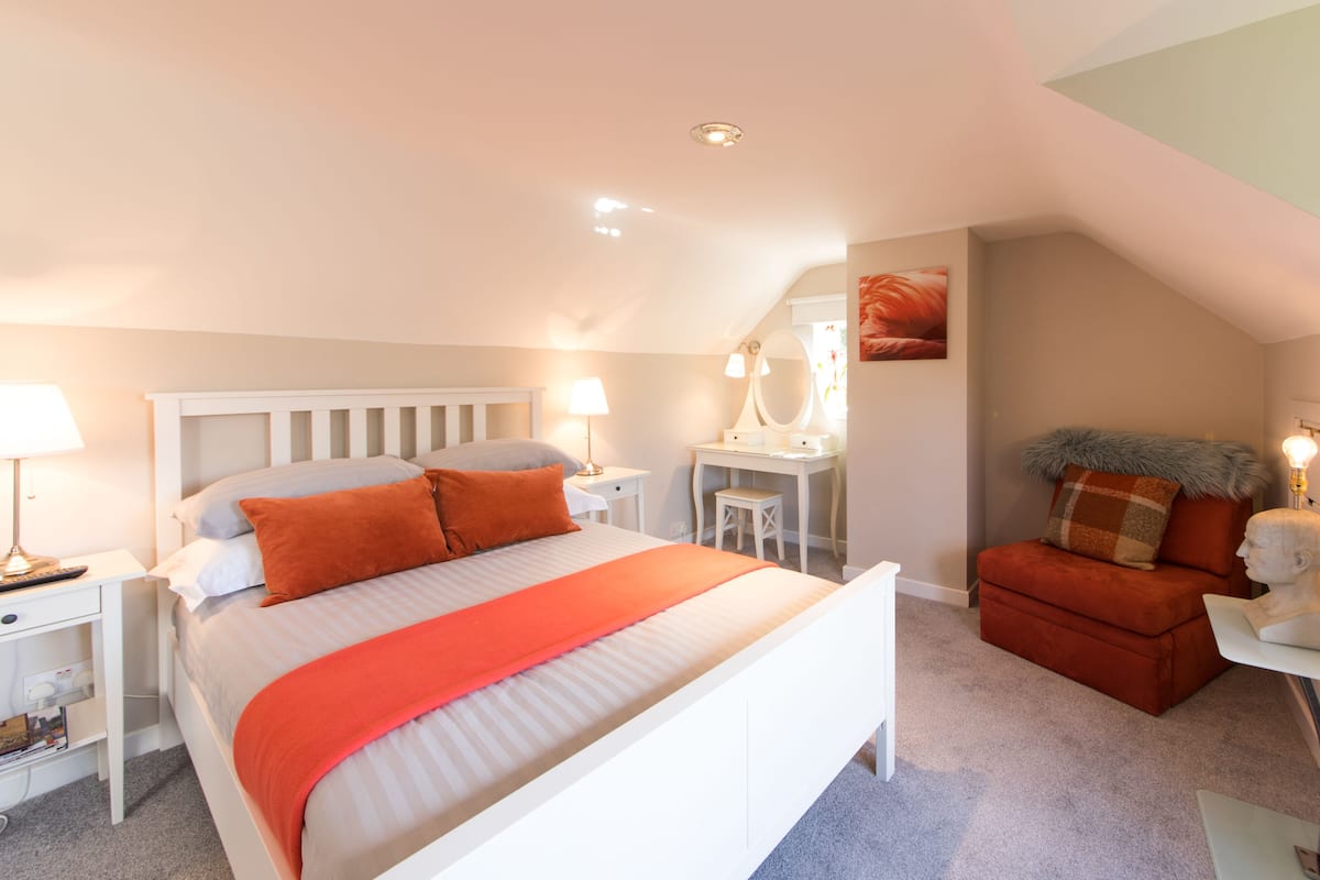 A bedroom with a bed, bedside tables, a desk, a chair, and a mirror.