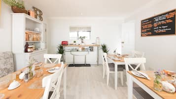 A bright, modern kitchen with white cabinetry, a central island, and a chalkboard menu listing breakfast items.