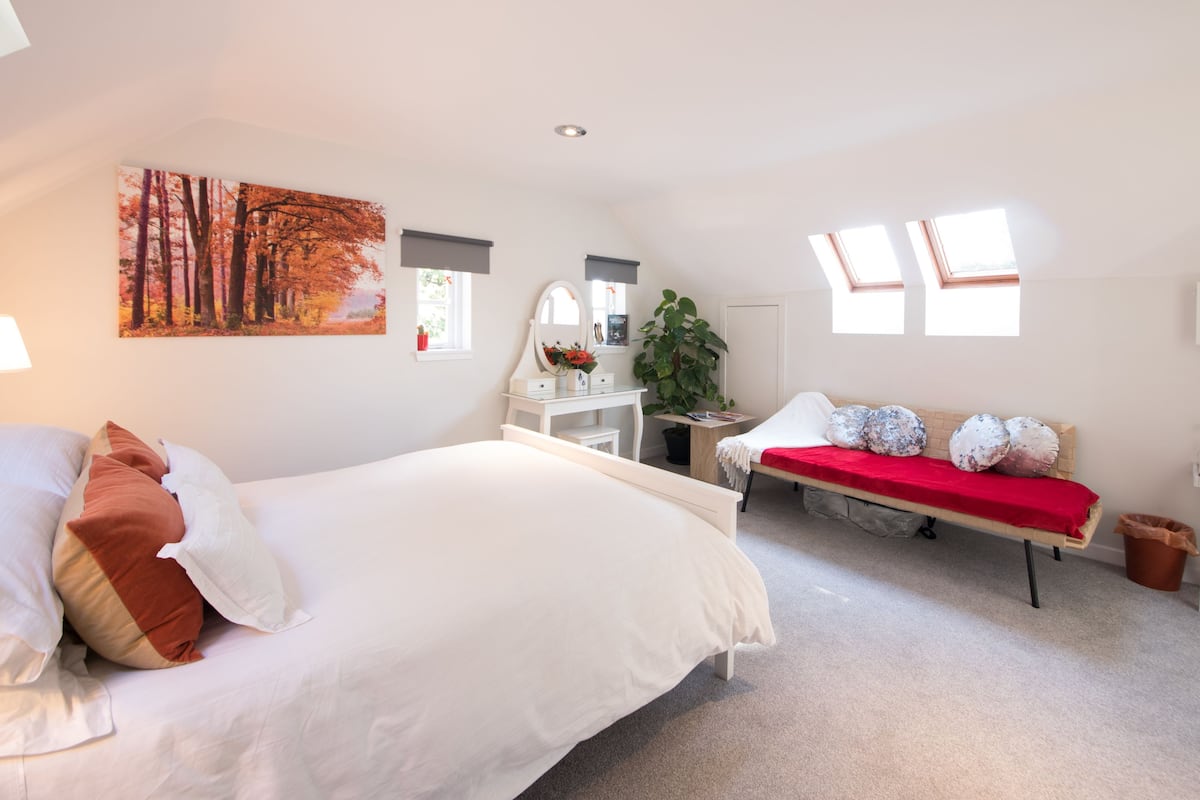 A bedroom with a large bed, a desk, and a red bench.