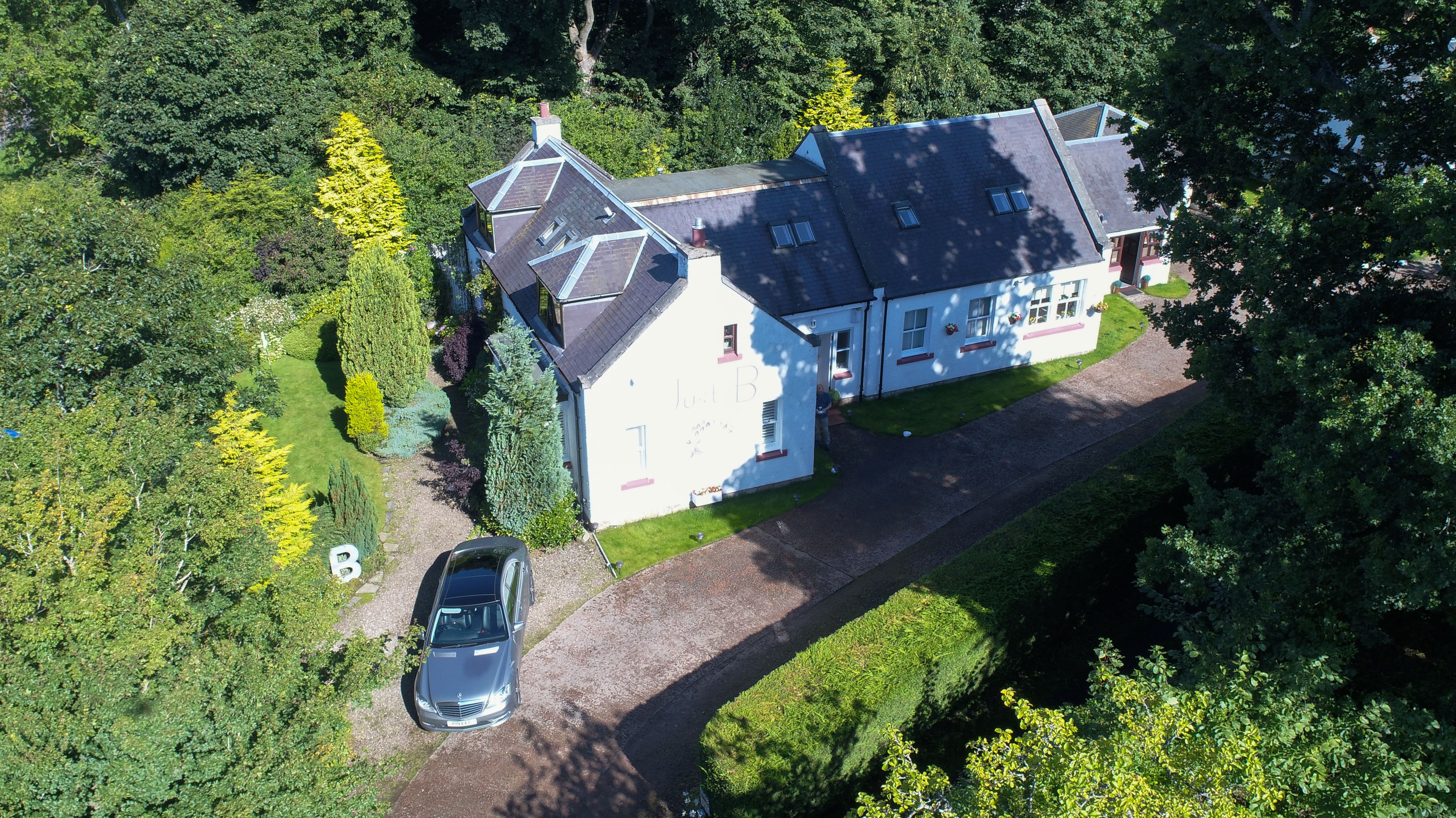An aerial view of a large house with a driveway and a parked car.