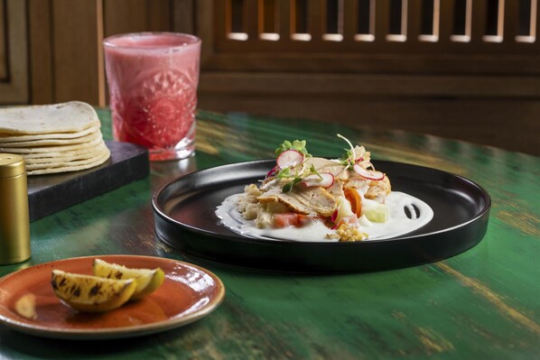 A table with a plate of food, a glass of drink, and a stack of tortillas.