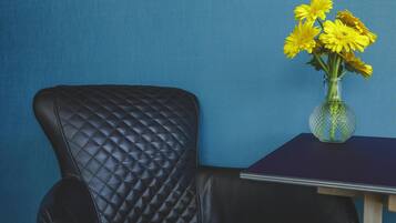 Ein schwarzer Ledersessel mit einer gesteppten Rückenlehne und ein kleiner Tisch mit einer Vase voller gelber Blumen vor einer blauen Wand.