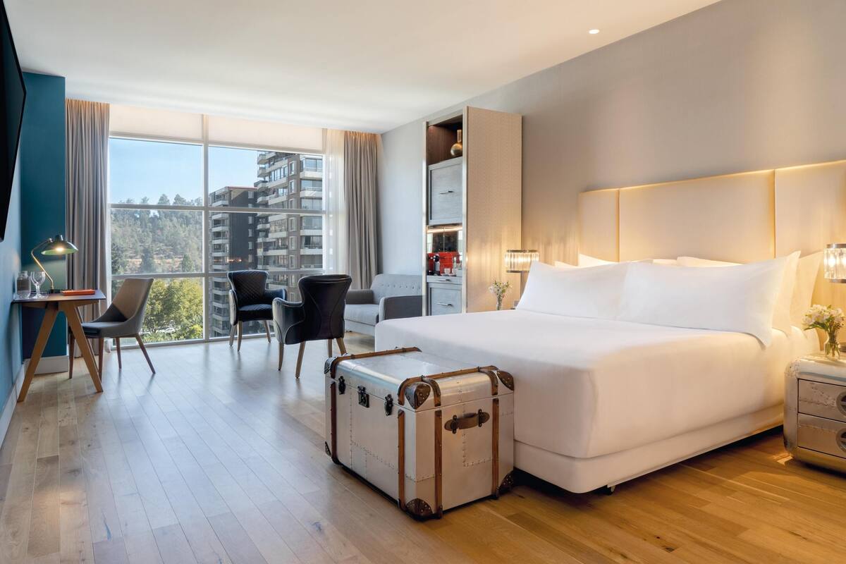Ein modernes Hotelzimmer mit einem großen Bett, einem Schreibtisch, einem Stuhl und einem Koffer.
