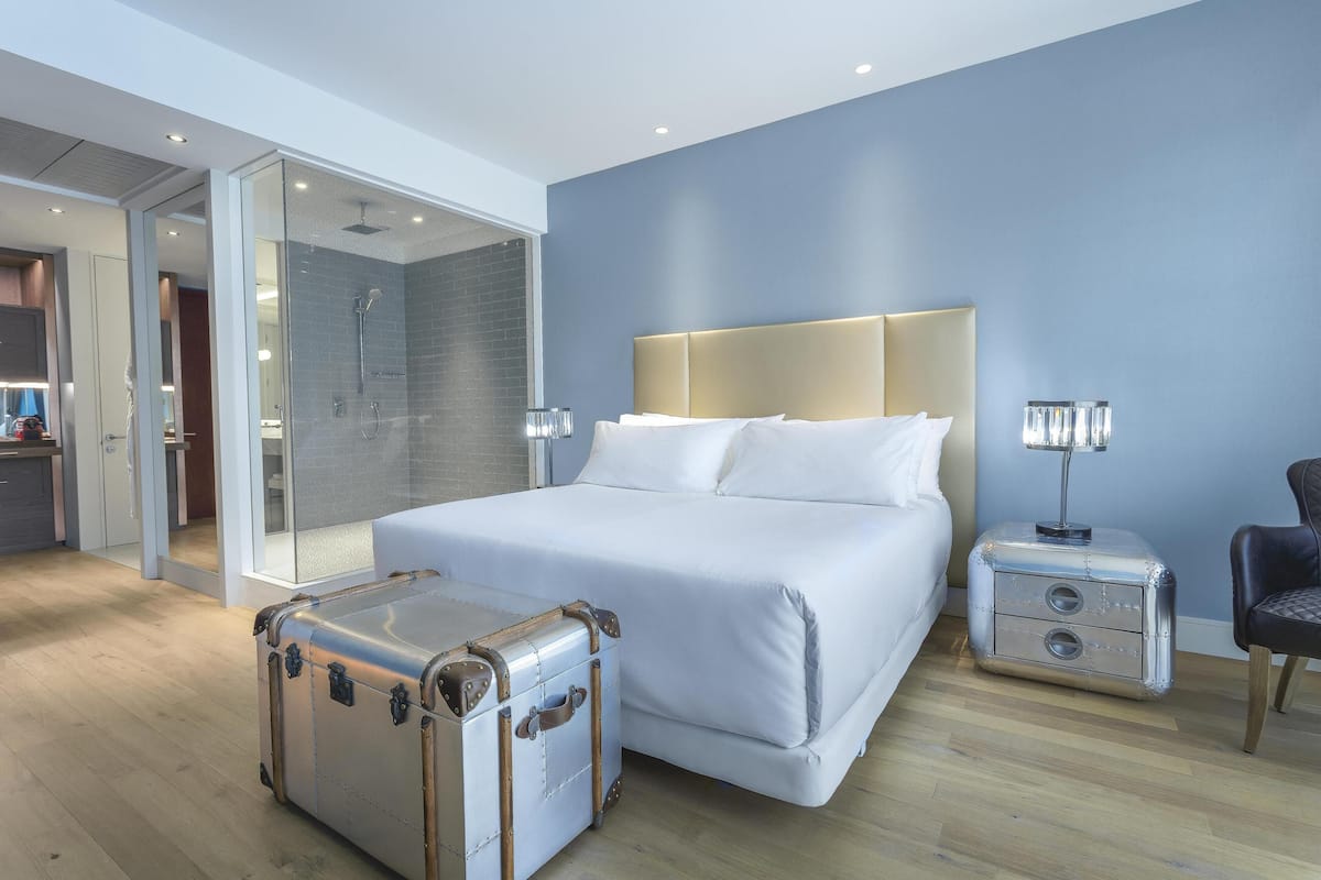 Ein modernes Hotelzimmer mit einem großen Bett, einem begehbaren Kleiderschrank, einer Duschkabine und einem Koffer auf dem Boden.
