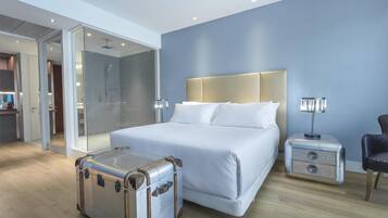 A modern hotel room with a large bed, a walk-in closet, a shower area, and a suitcase on the floor.