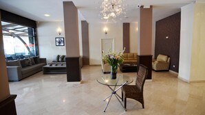 A spacious living area with a modern chandelier, a glass coffee table, and a comfortable seating arrangement including a sofa and armchairs.