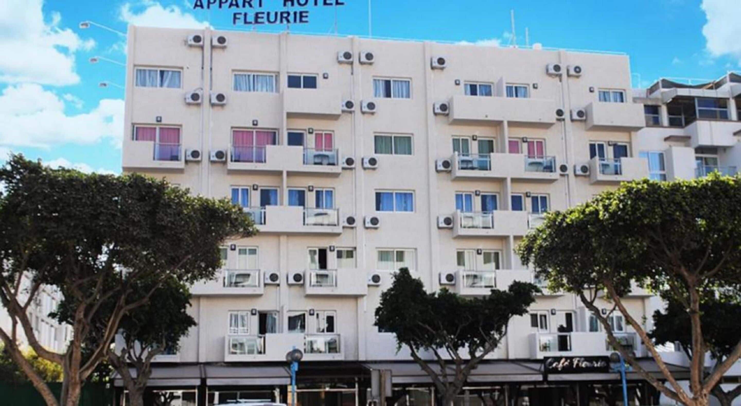 A multi-story building with balconies, air conditioning units, and a sign reading "APART HOTEL FLEURIE".