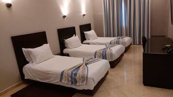 Ein Hotelzimmer mit drei Einzelbetten, einem Schreibtisch und einem Stuhl.