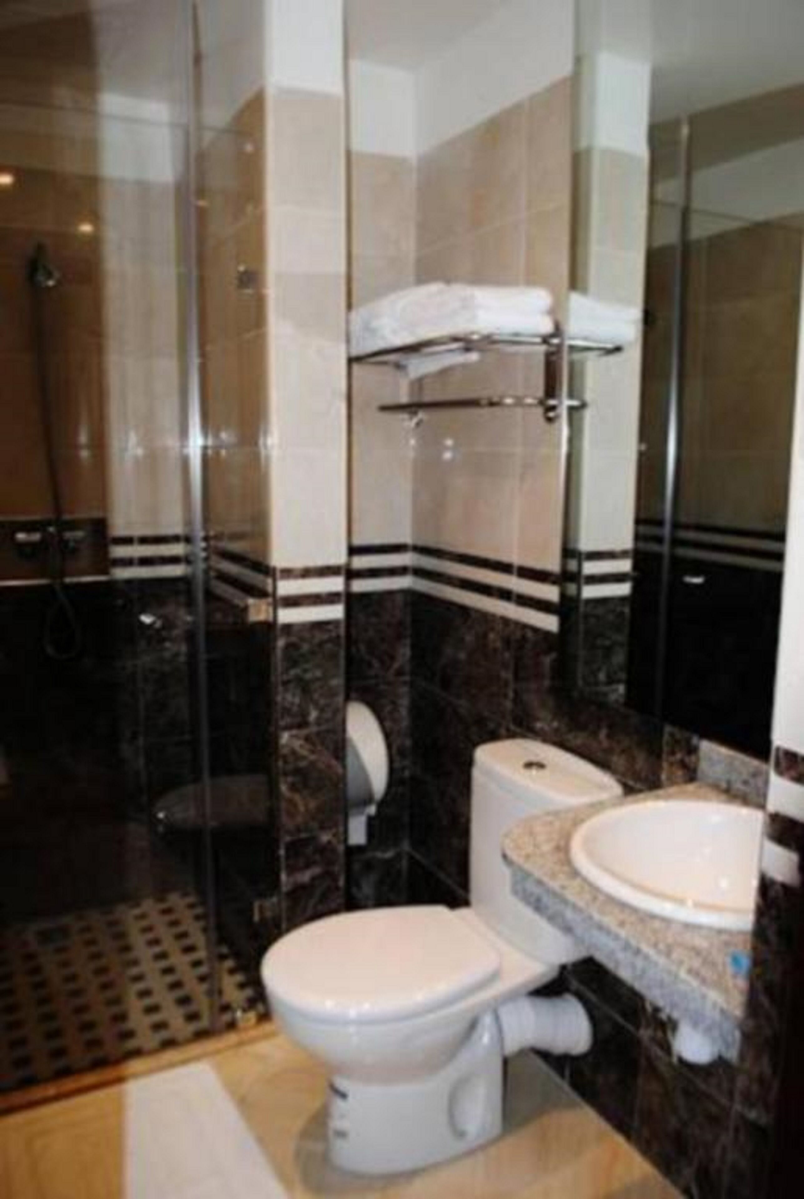 A bathroom with a glass shower enclosure, a toilet, and a sink with a marble countertop.