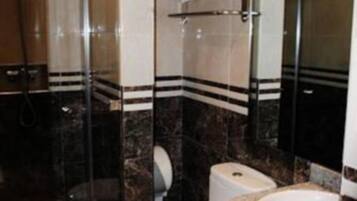 A bathroom with a glass shower enclosure, a toilet, and a sink with a marble countertop.