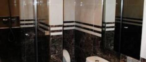 Een badkamer met een douchecabine van glas, een toilet en een wastafel met een marmeren aanrechtblad.