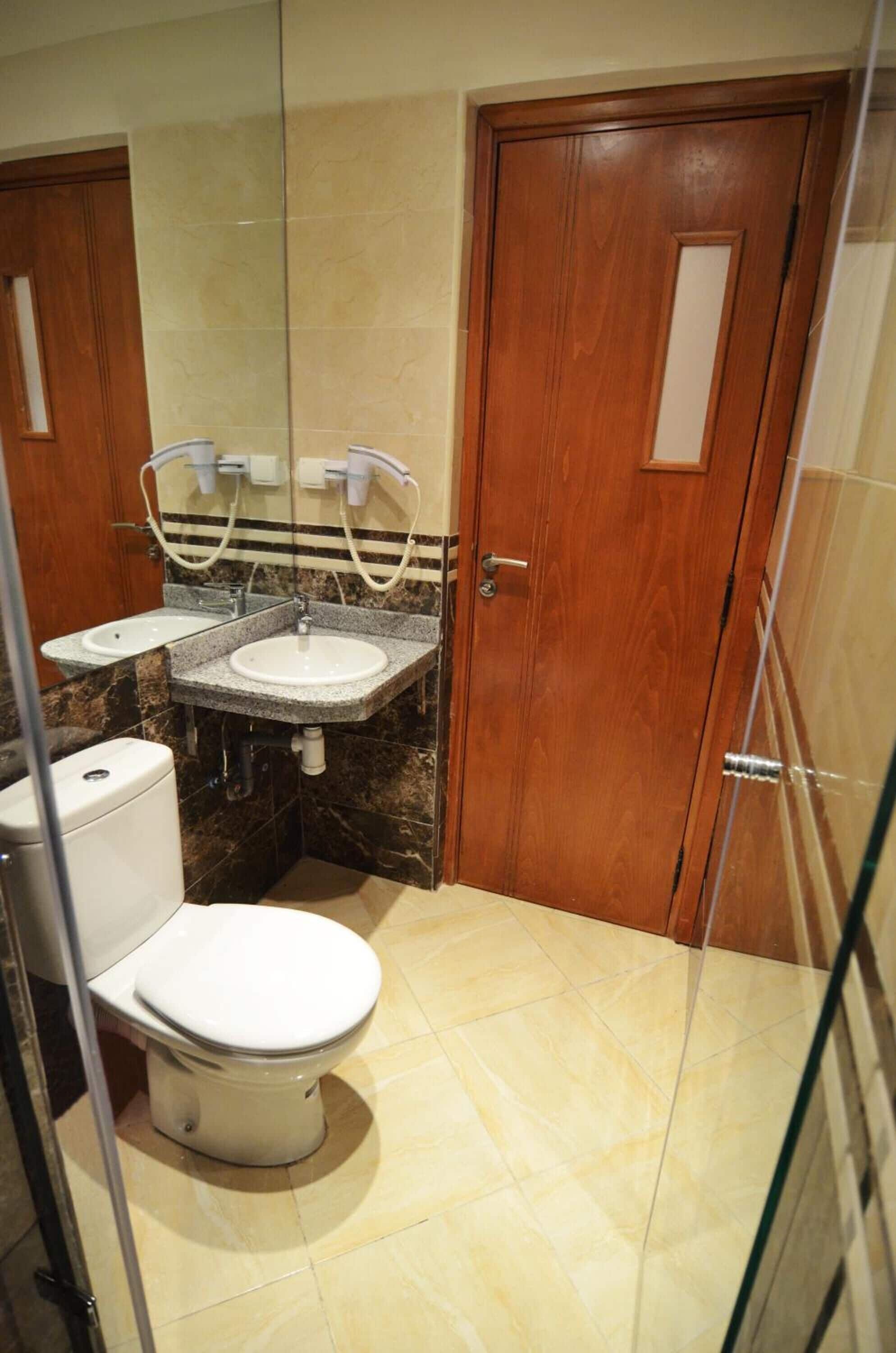 A compact bathroom with a toilet, two sinks, and a mirror.