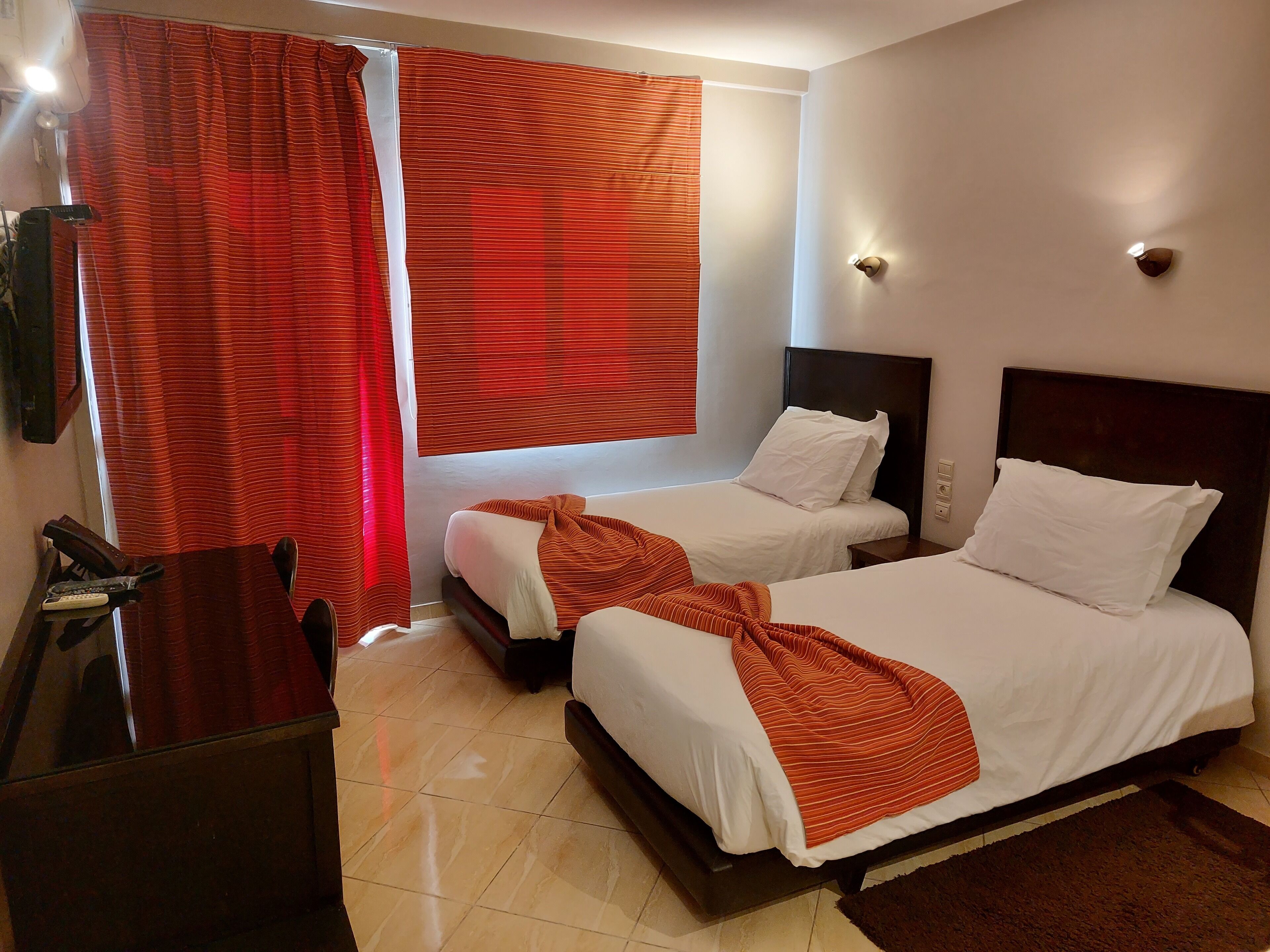 A hotel room with two beds, a desk, and a window with curtains.