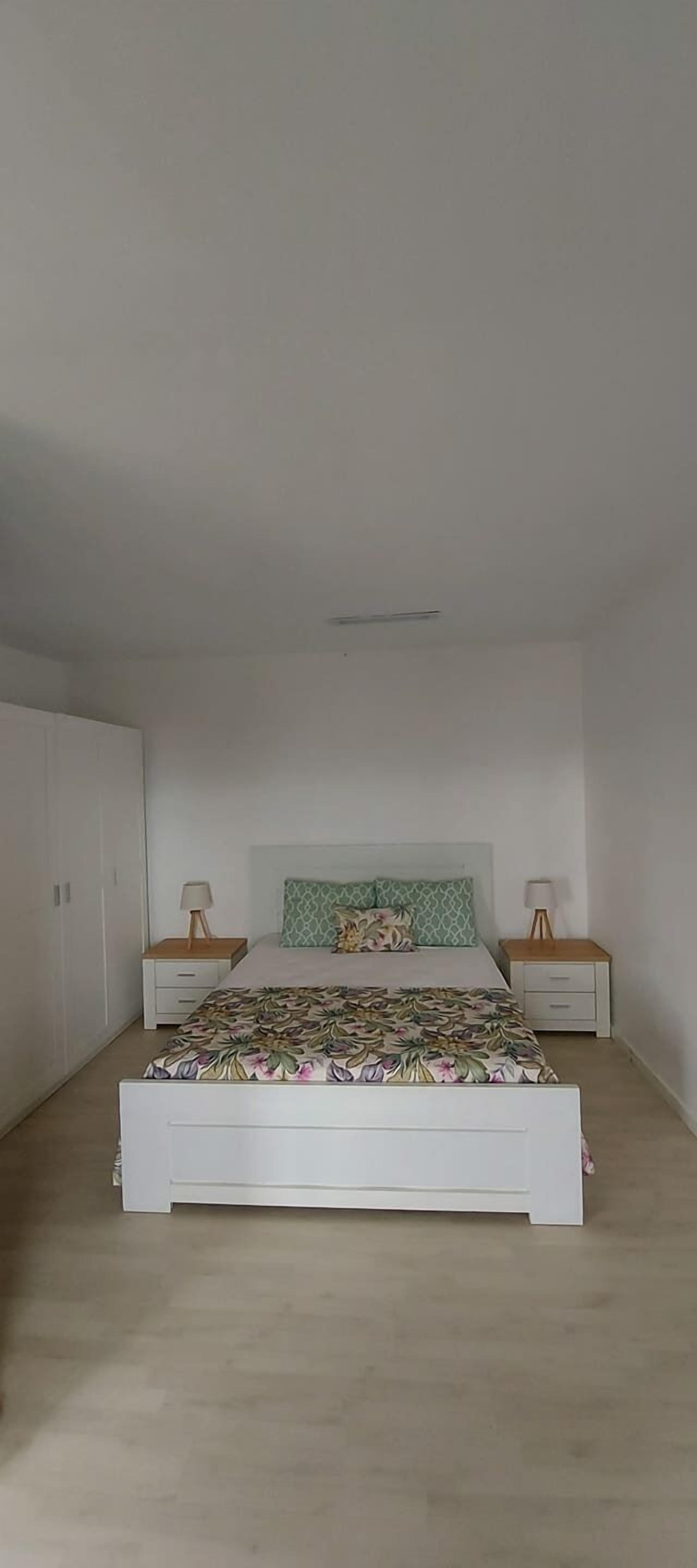 A bedroom with a bed, two bedside tables, a wardrobe, and a ceiling fan.