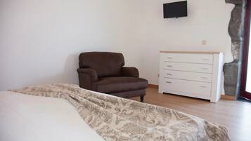 A bedroom with a bed, a brown armchair, a white dresser, and a stone accent wall.