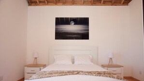 A bedroom with a bed, two bedside tables, a nightstand, a wall-mounted artwork, and a wooden ceiling. - Sara Village (Sao Roque do Pico)