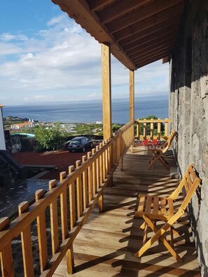 A wooden deck with a railing overlooking a scenic view of the ocean and a town. - Sara Village (Sao Roque do Pico)