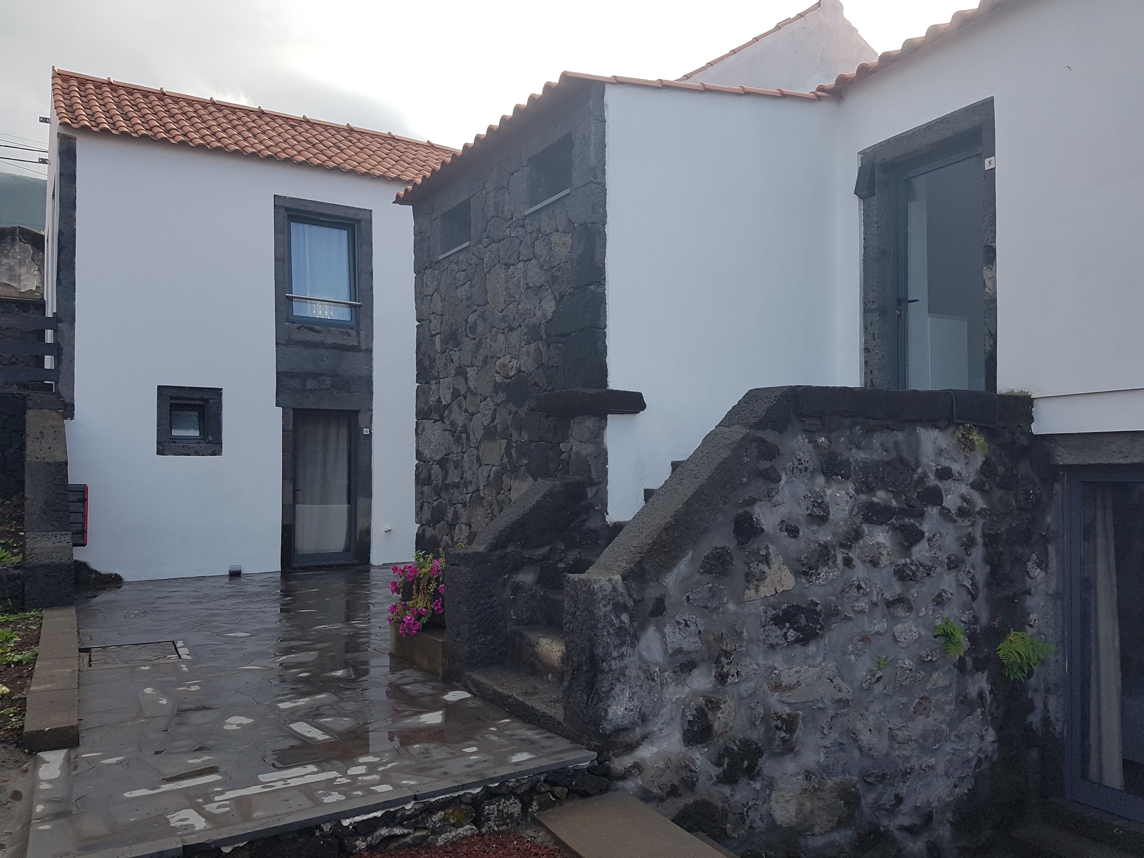A courtyard with a wet stone floor, a white building with a tiled roof, and a stone wall.
