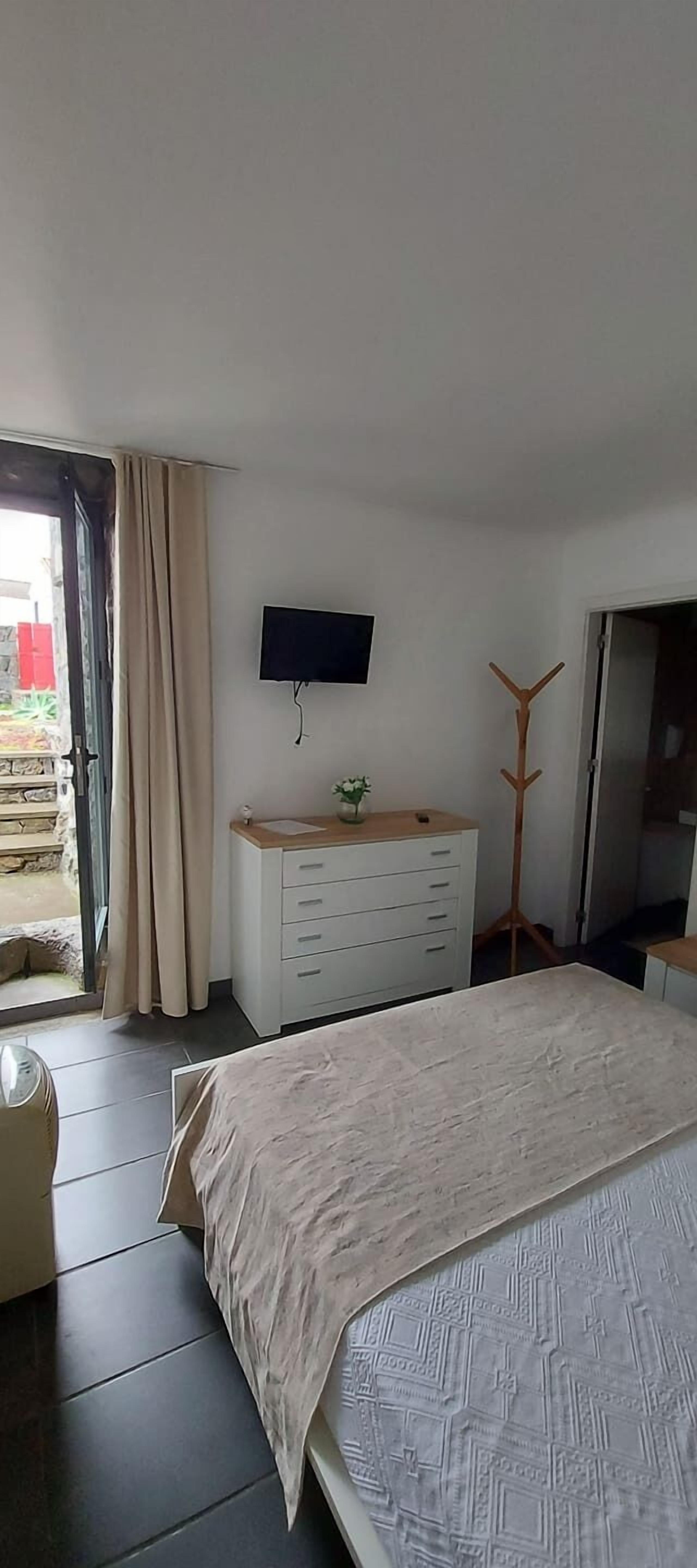 Un dormitorio con cama, cómoda, televisor en la pared y puerta que da a un balcón.