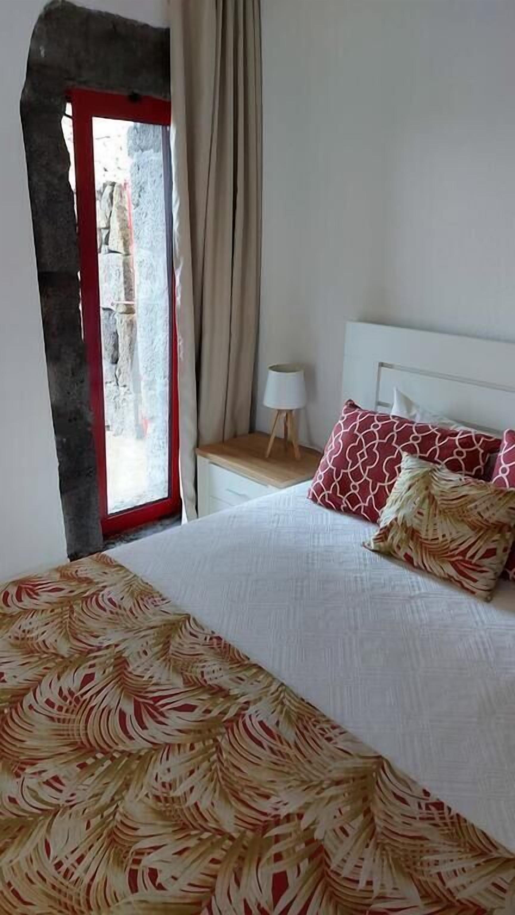 A bedroom with a bed, a nightstand, a lamp, and a view through a window with curtains.