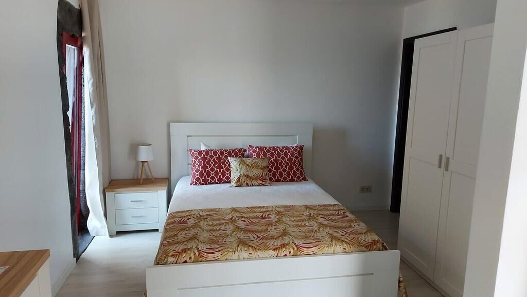 Een slaapkamer met een bed, nachtkastje, kledingkast en een raam met gordijnen.