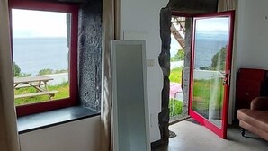 A room with a large window, a sliding glass door, and a wooden floor. - Sara Village (Sao Roque do Pico)