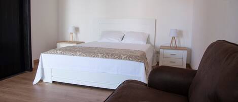 Un dormitorio con una cama, dos mesitas de noche con lámparas, un sillón de cuero marrón y suelo de madera.