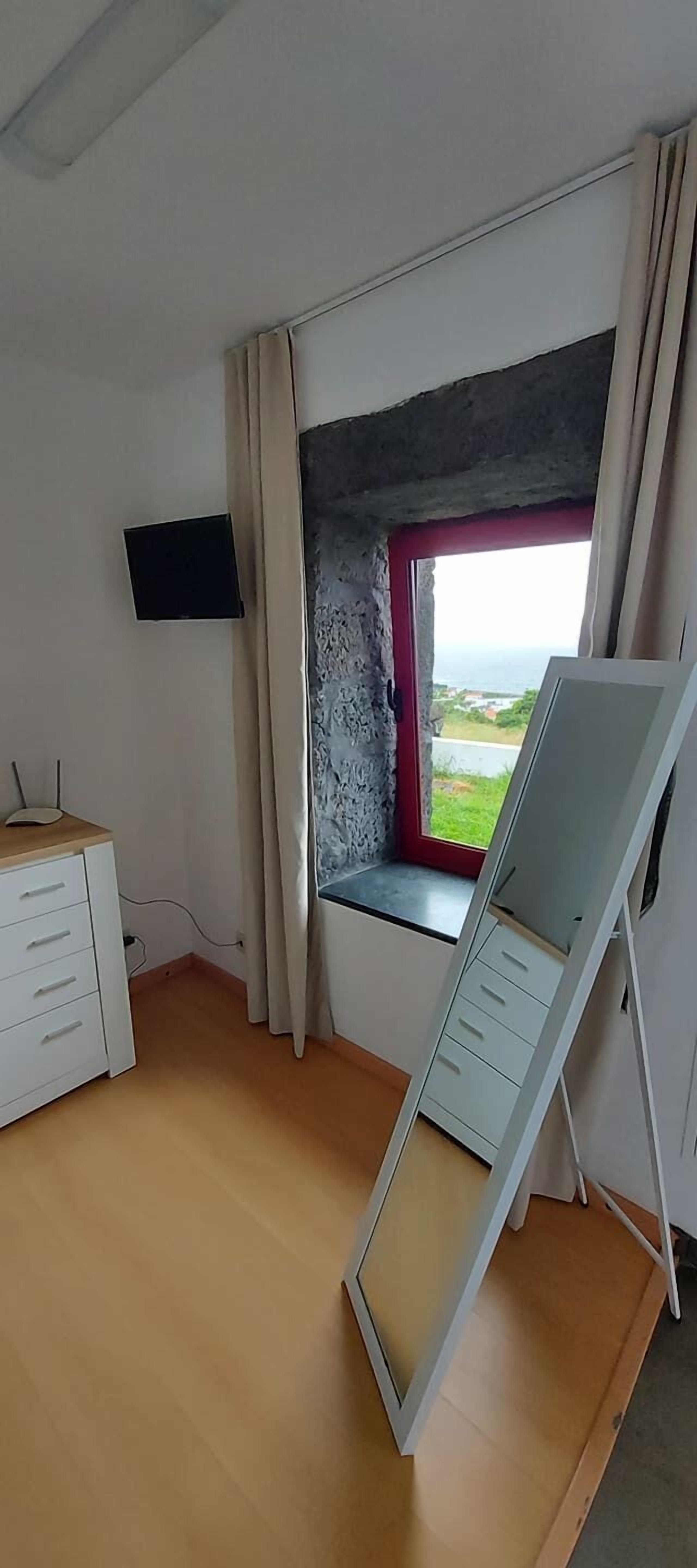 A room with a window, a desk, and a flat-screen TV mounted on the wall.