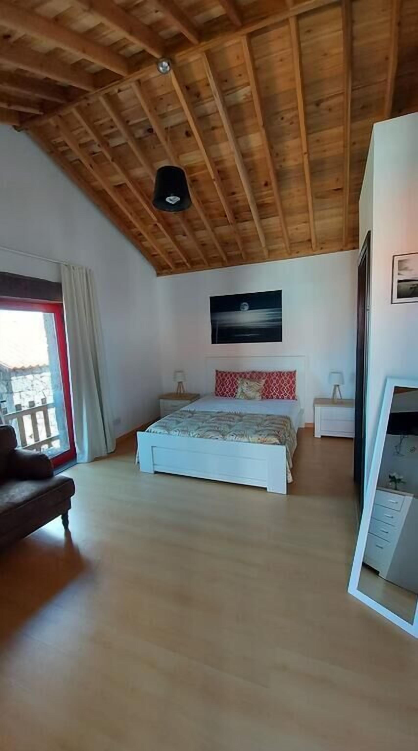 A bedroom with a wooden ceiling, a bed with a red and white pillow, a nightstand, a dresser, and a large mirror.