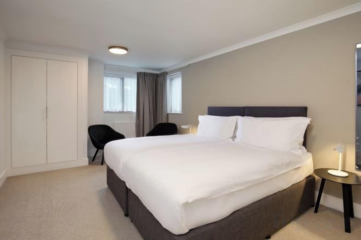 A hotel room with a large bed, a chair, a bedside table, and a wardrobe.