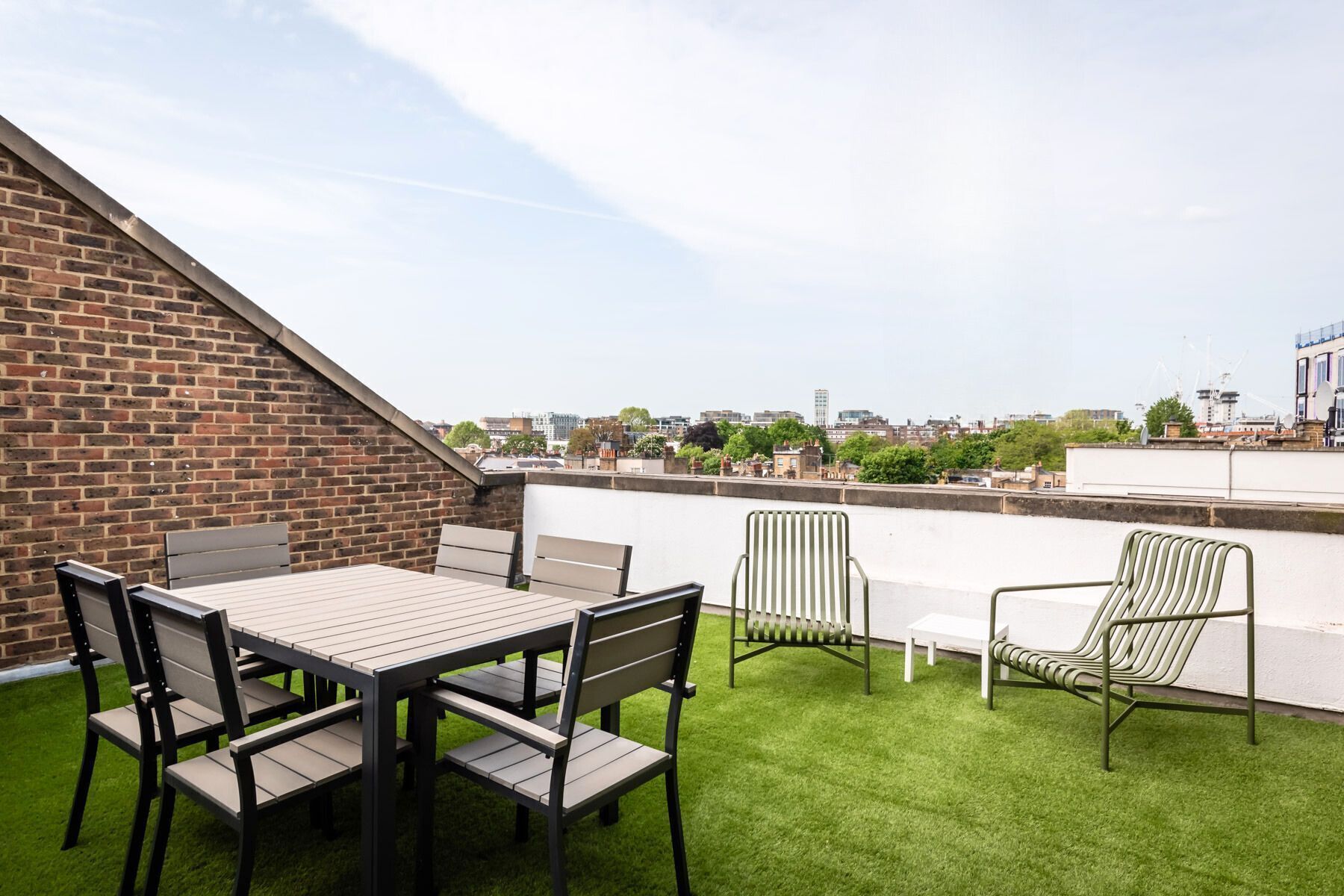 A rooftop terrace with a brick wall, a table with chairs, and a view of the cityscape.