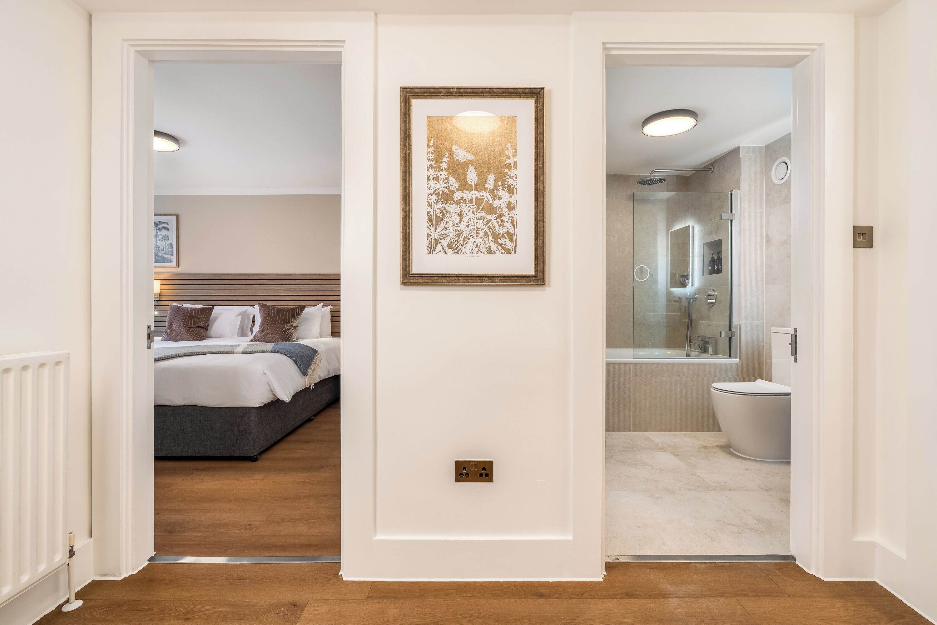 A hallway leading to a bedroom with a bed and a bathroom with a shower and toilet.