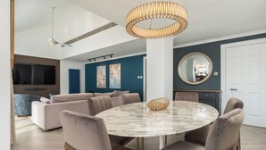 A modern living room with a round marble table, beige sofas, a ceiling fan, and a large TV. - Monarch House Serviced Apartments (London)