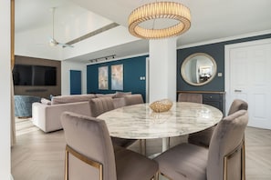 A modern living room with a round marble table, beige sofas, a ceiling fan, and a large TV.