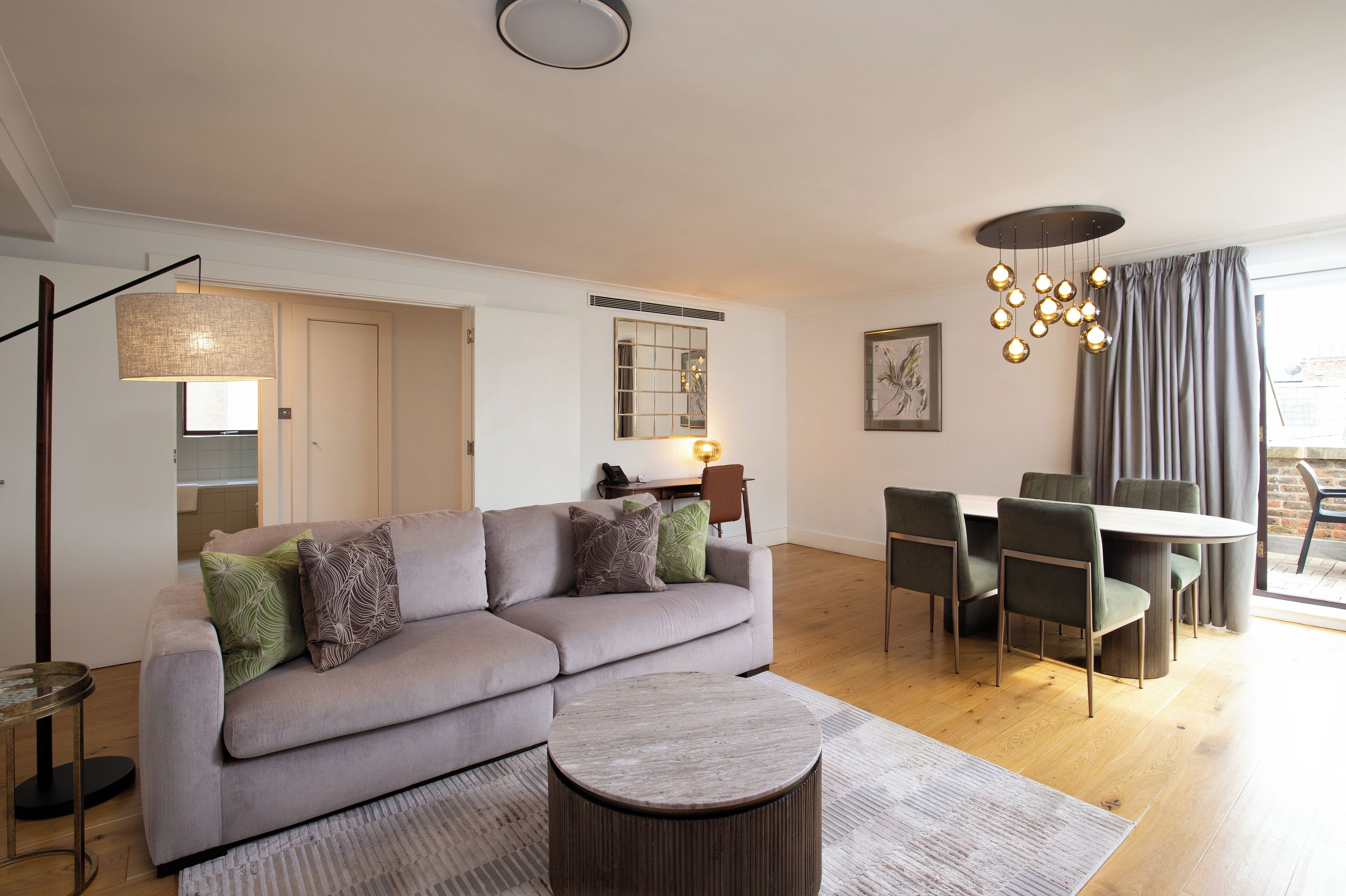 Uma sala de estar moderna com um sofá cinzento, uma mesa de centro redonda e uma área de jantar com mesa e cadeiras de madeira.