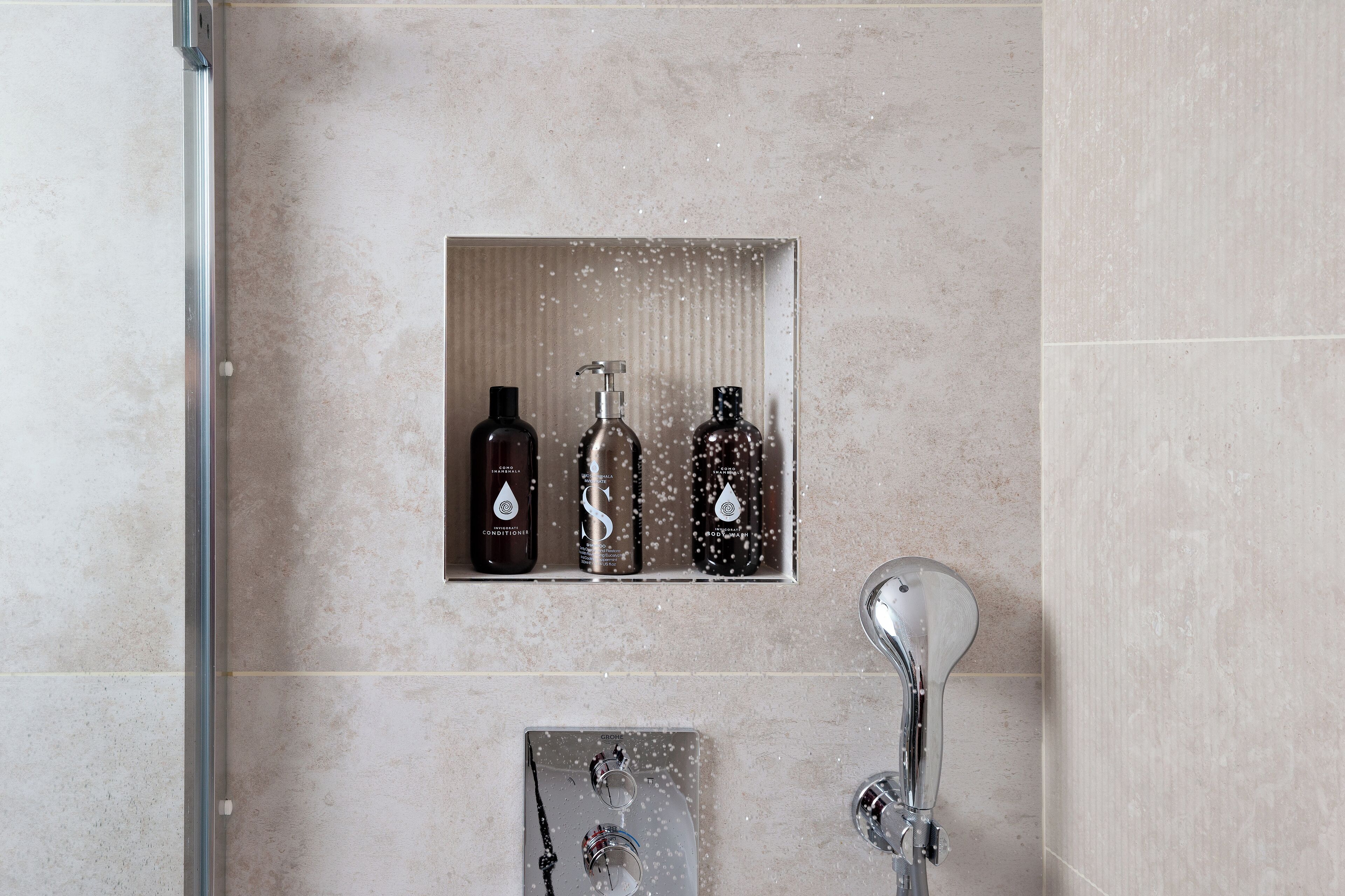 A shower area with a glass-enclosed shelf holding three bottles of shampoo and conditioner.