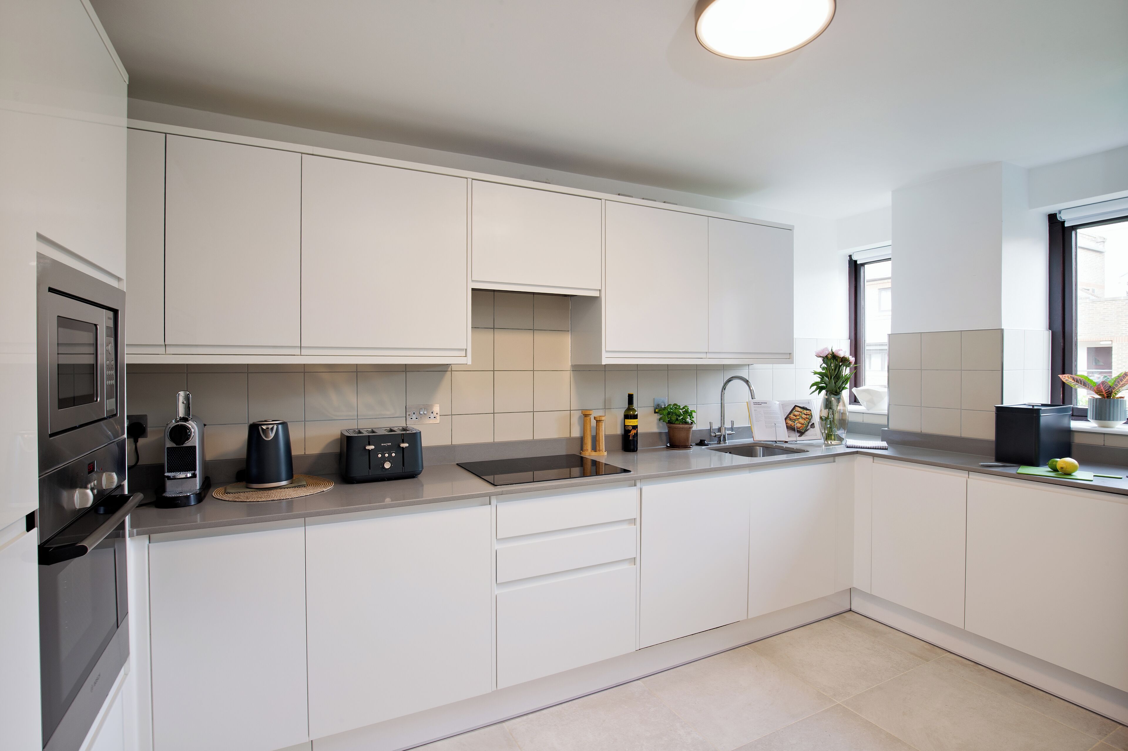 A modern kitchen with white cabinets, a built-in oven, a coffee maker, and a sink.