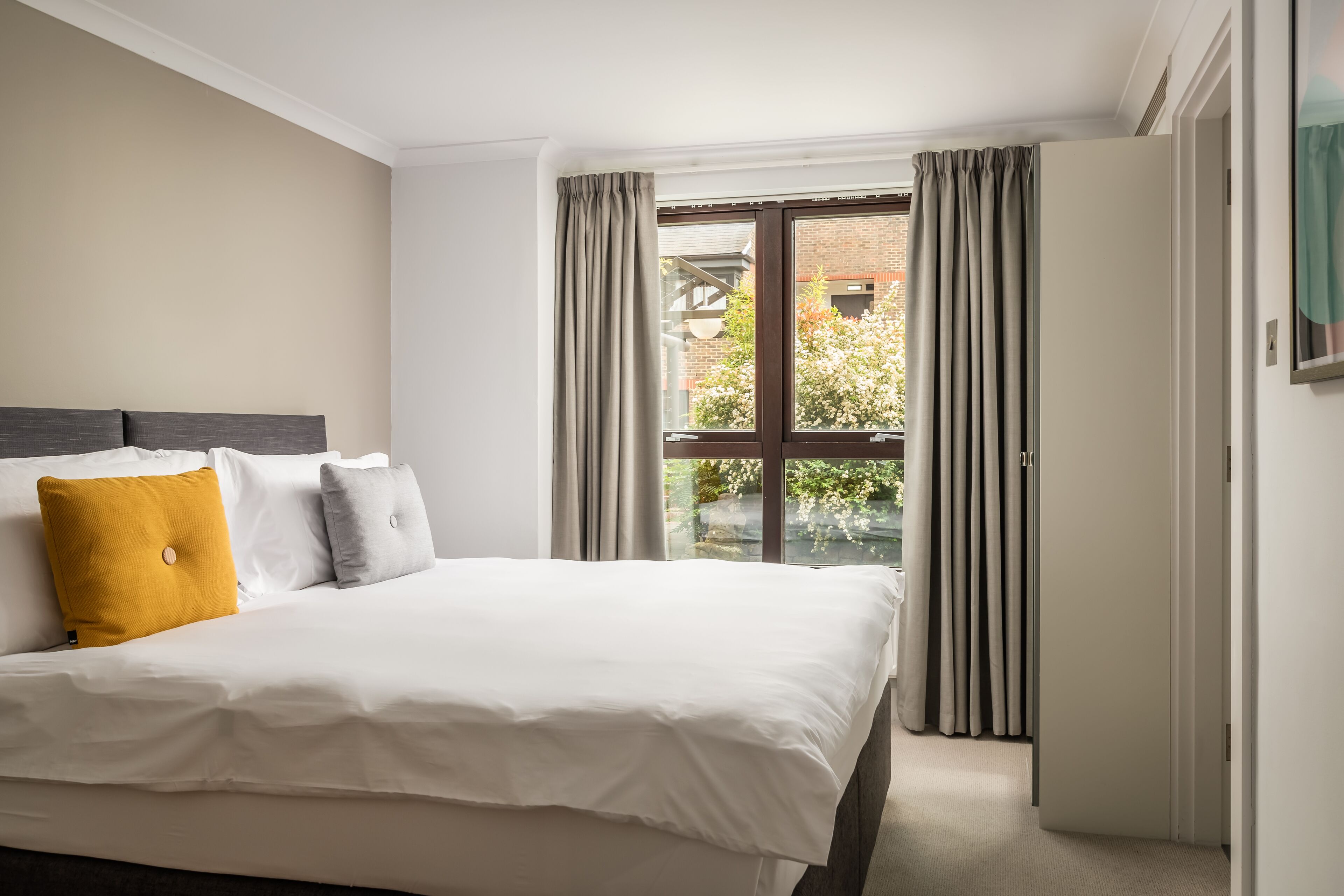 A hotel room with a large bed, a window with curtains, and a view of the outside.