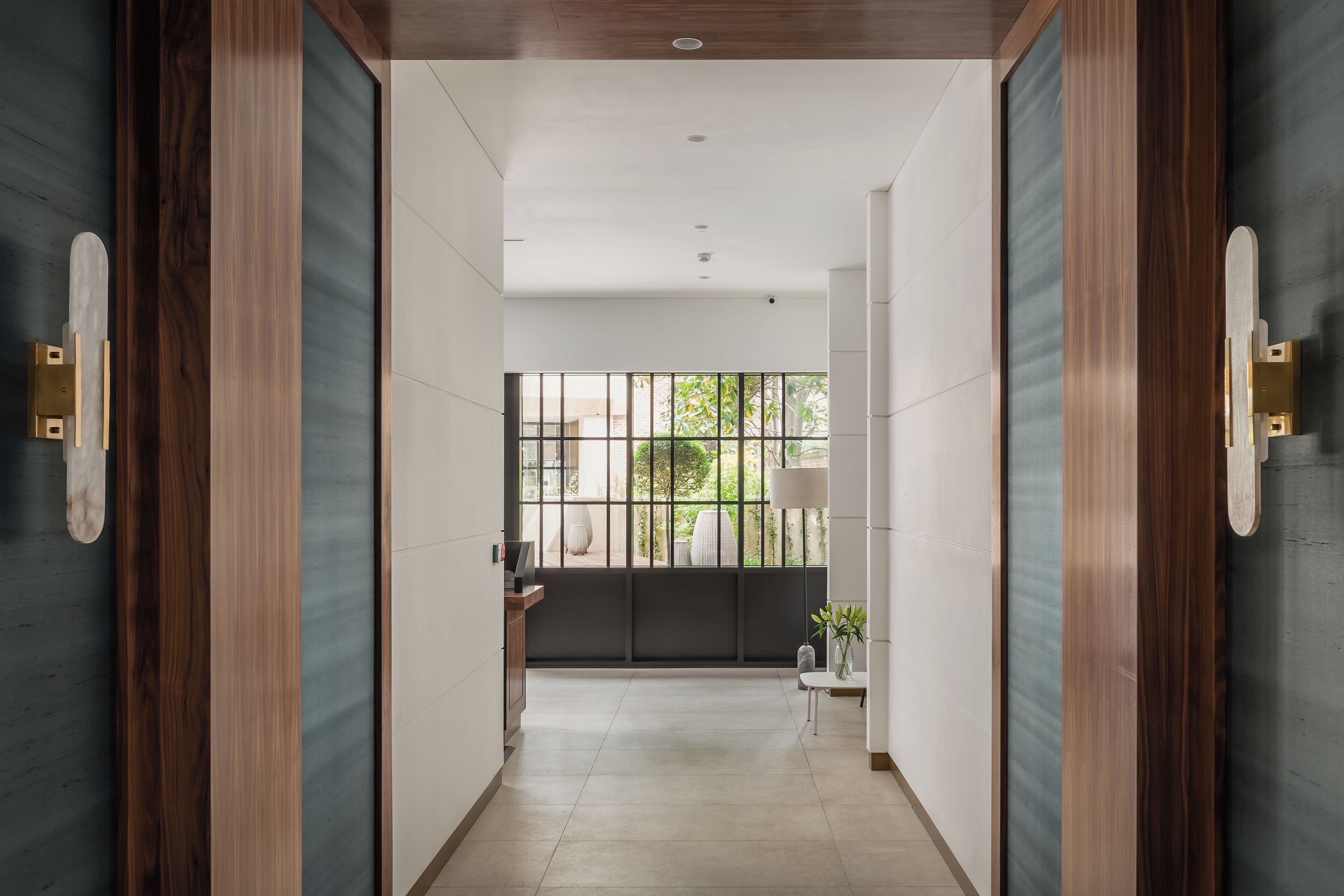 A hallway with a view of a balcony, a small table with a plant, and a door with a wooden frame.