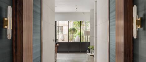 A hallway with a view of a balcony, a small table with a plant, and a door with a wooden frame.