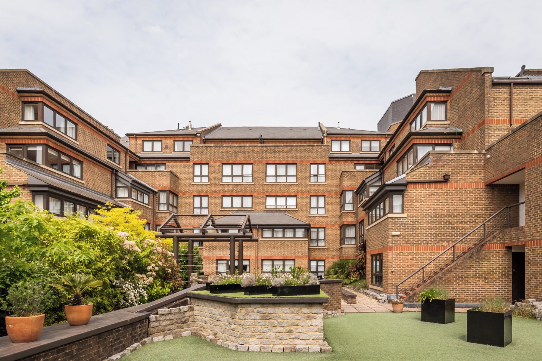A multi-story residential building with a courtyard featuring a stone wall, potted plants, and a small garden area.