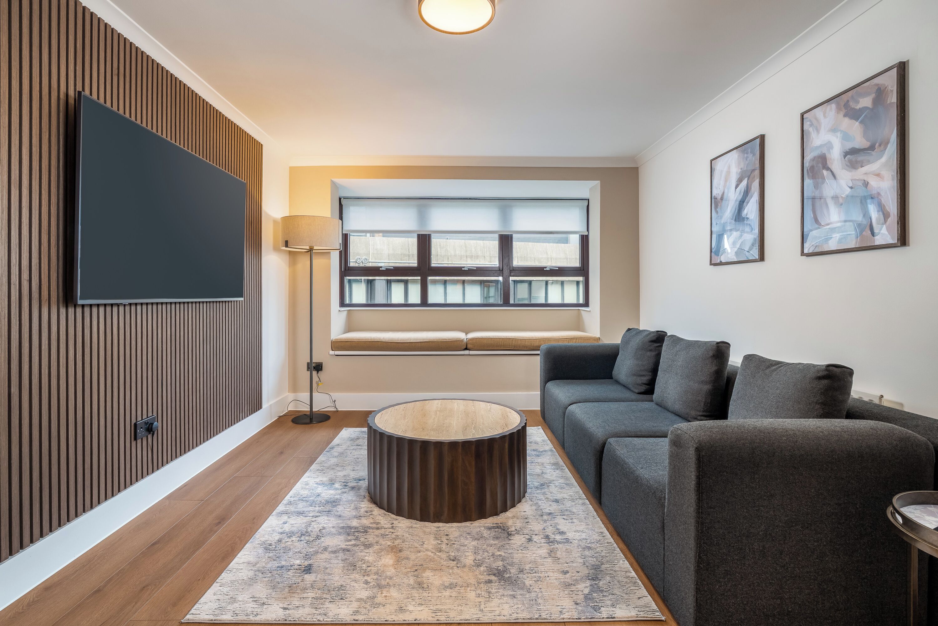 A modern living room with a flat-screen TV, a sofa, a coffee table, and a window with blinds.