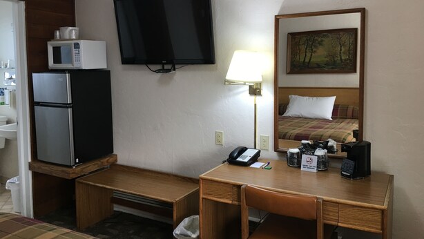 Habitación de hotel con cama, escritorio, teléfono, cafetera y microondas sobre un mueble.