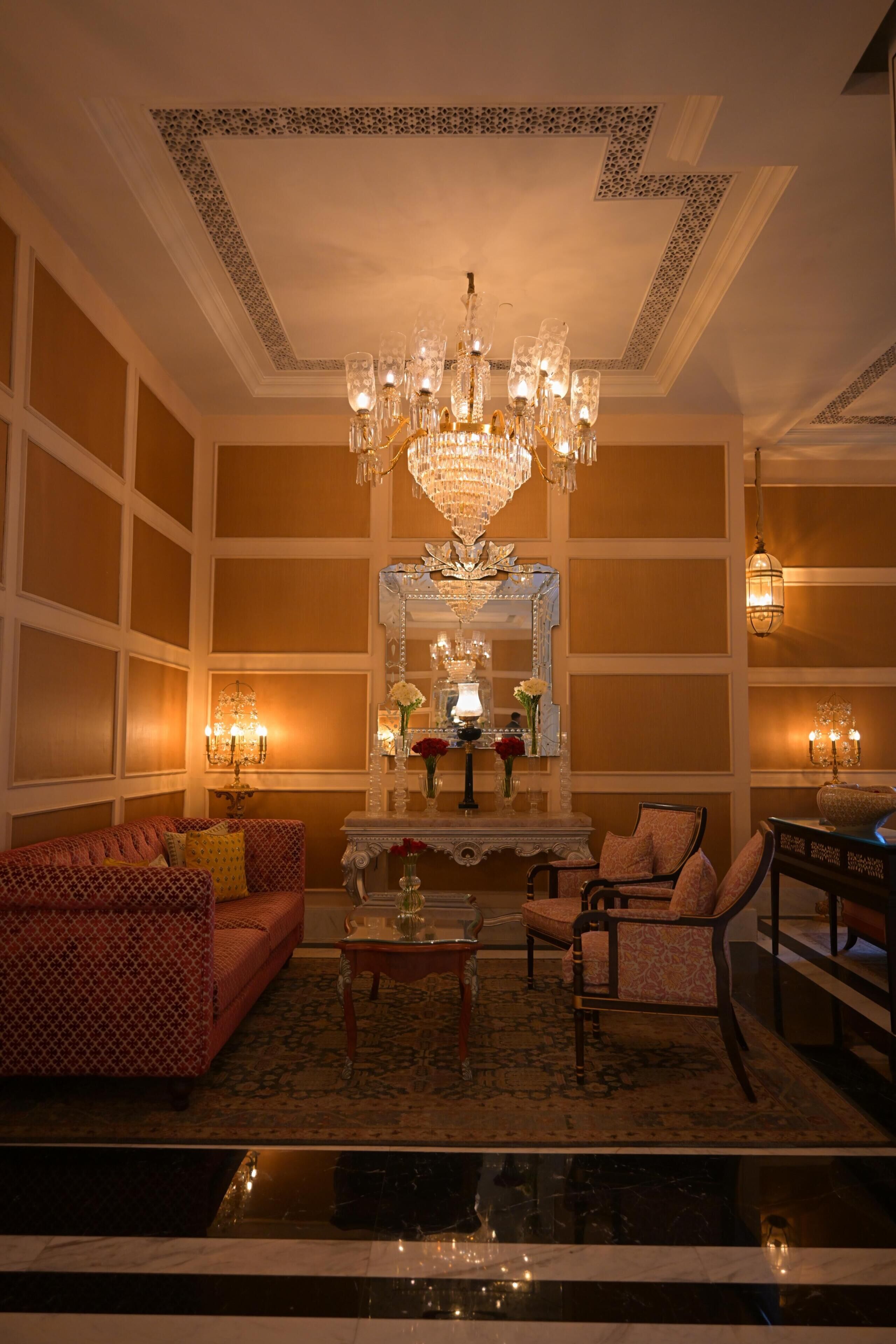 A room with a chandelier, a sofa, a chair, a table, and a mirror.