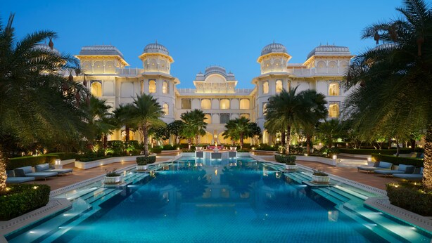 A large, well-lit swimming pool with a symmetrical design, surrounded by palm trees and lounge areas.