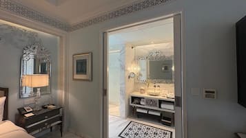 Ein Hotelzimmer mit Bett, Nachttisch, Lampe sowie einem Badezimmer mit Waschbecken, Spiegel und Handtuchhalter.