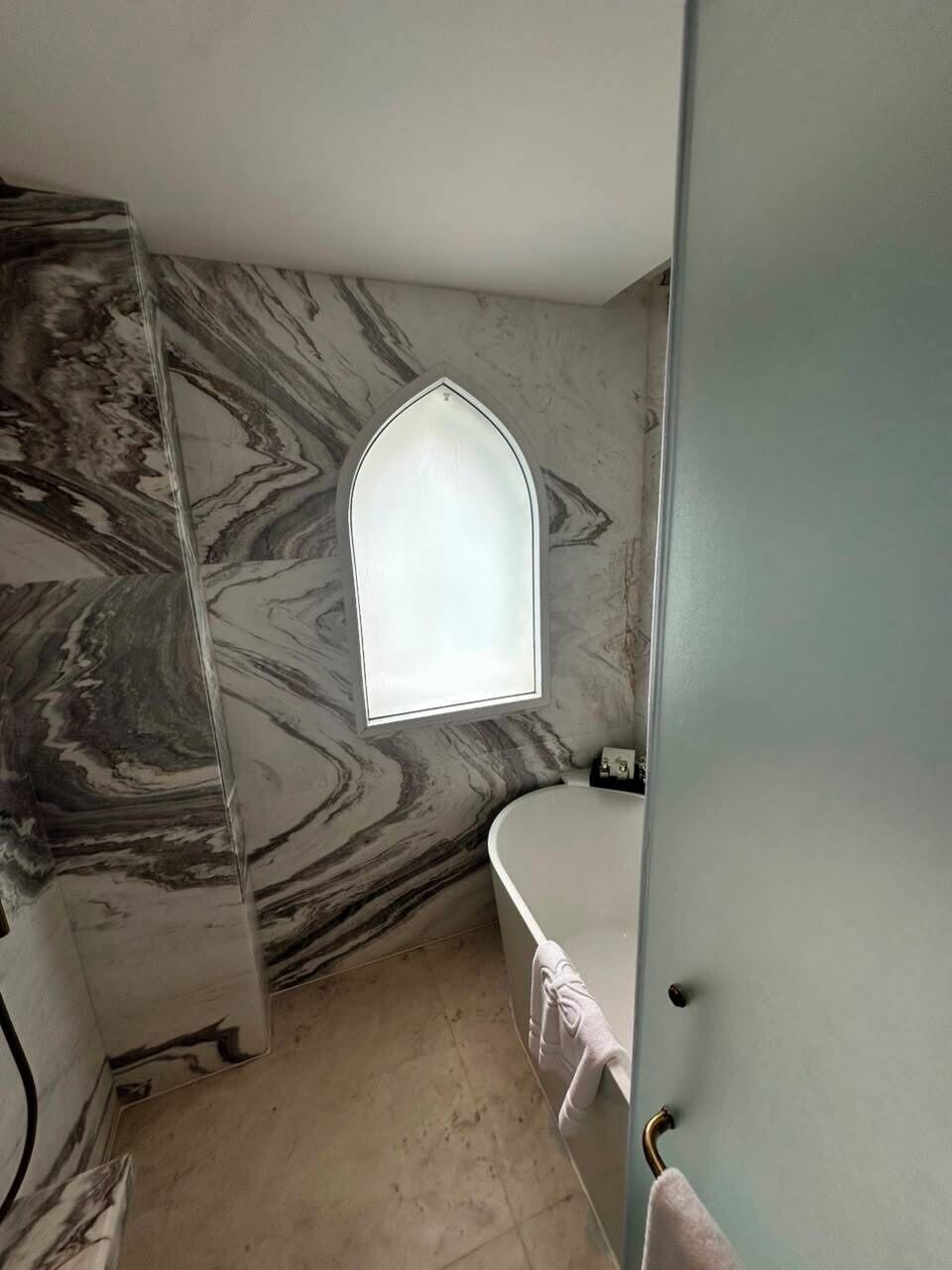Une salle de bain avec un mur en marbre, une baignoire blanche et une petite fenêtre.